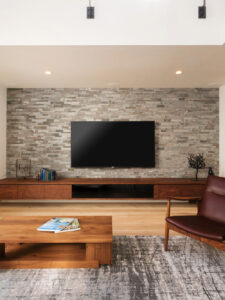 天然石タイルの壁にかかるTVとウォールナットのTVボード